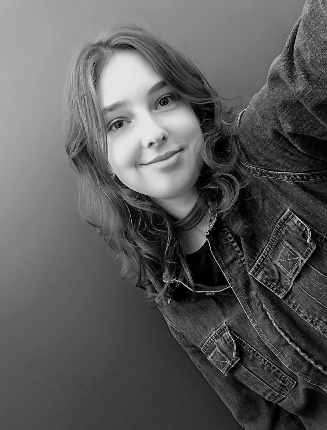 Photo of a woman in her late twenties with slightly curly hair, wearing a jeans shirt